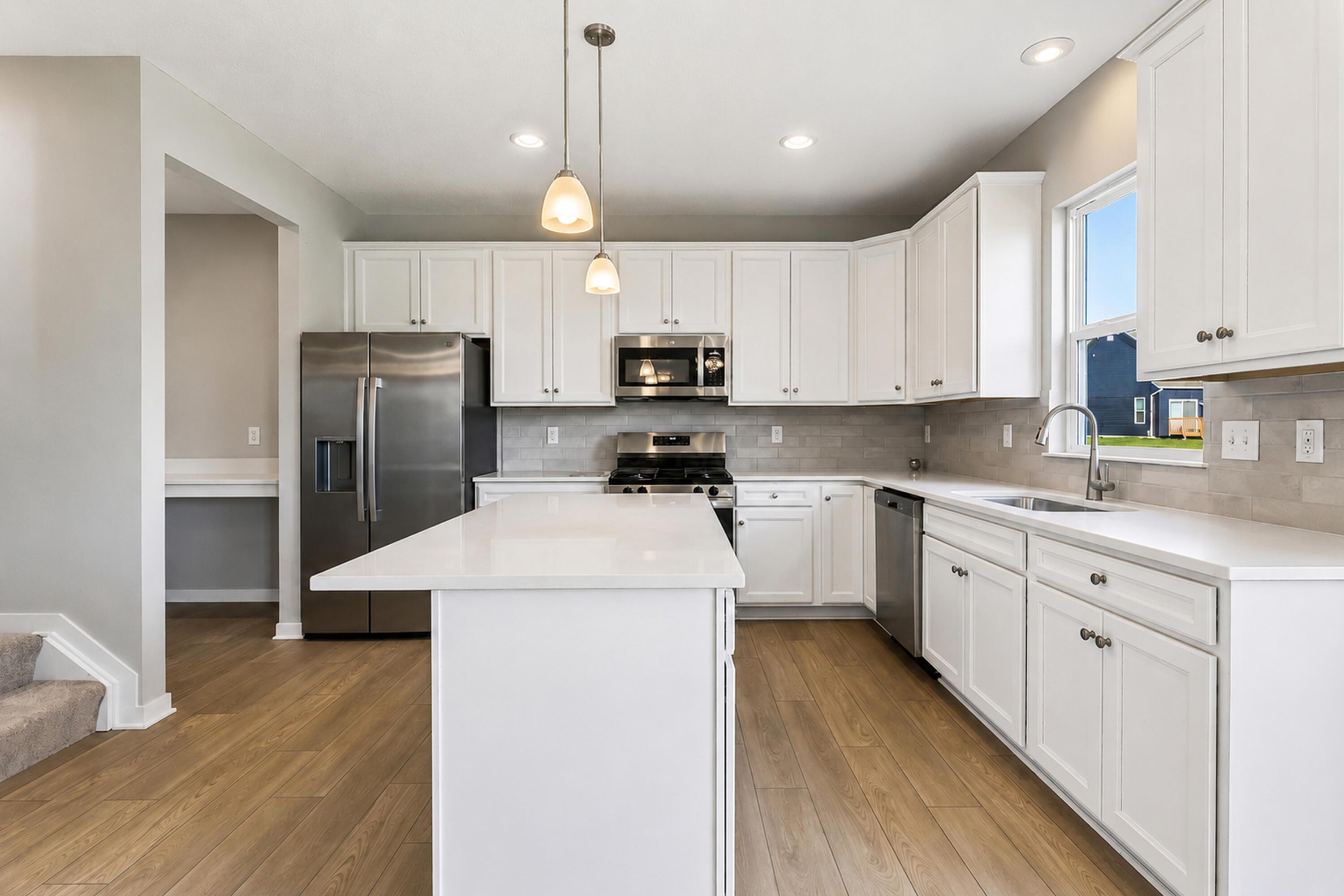Bright kitchen with white cabinets, stainless steel appliances, a large island, and wood-look flooring.