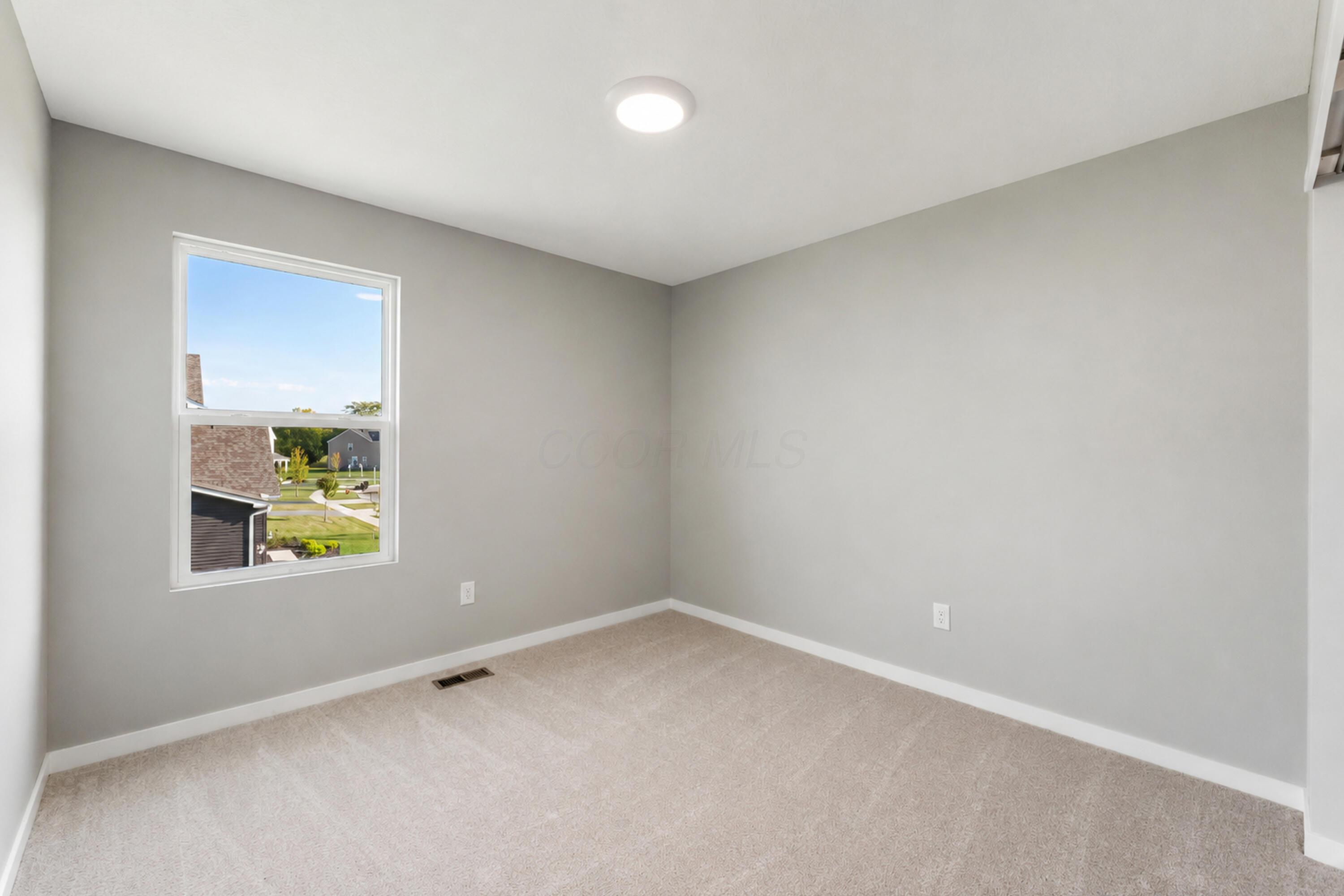 Empty carpeted room with gray walls and a window overlooking neighboring homes.