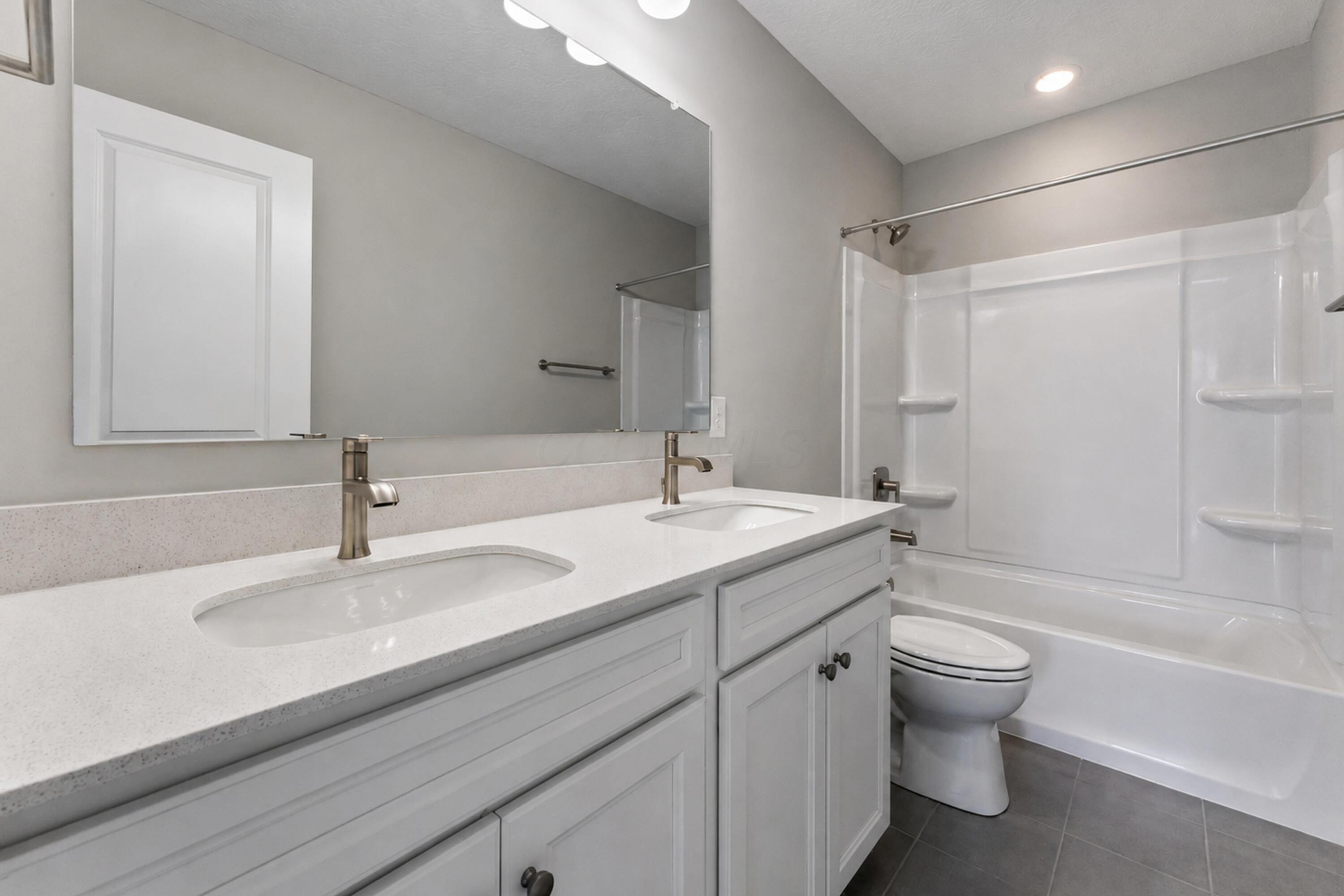 Bathroom with a double-sink vanity and a white tub-shower enclosure with built-in shelves.