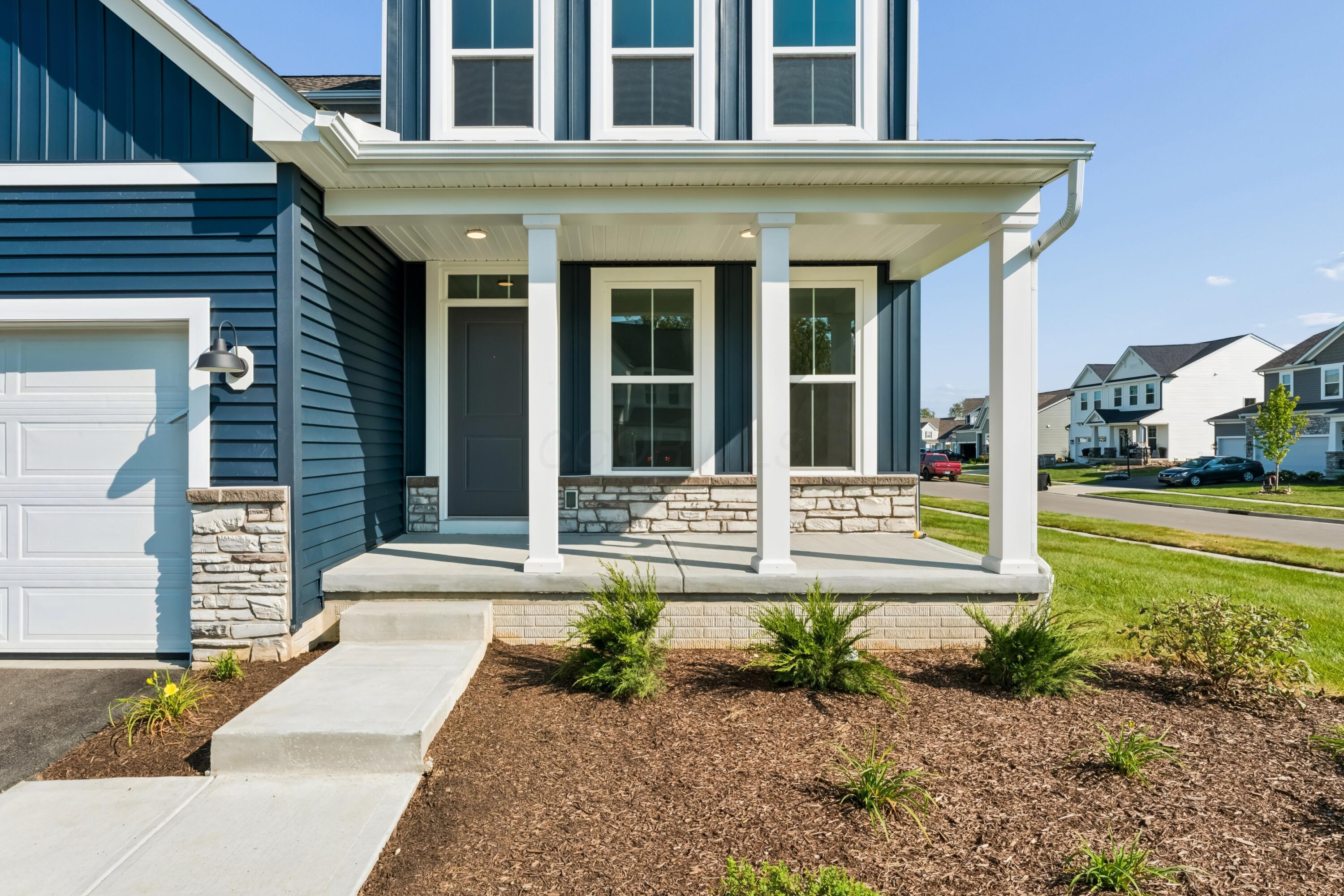 Blue house with a covered front porch, stone accents, and landscaped entry.