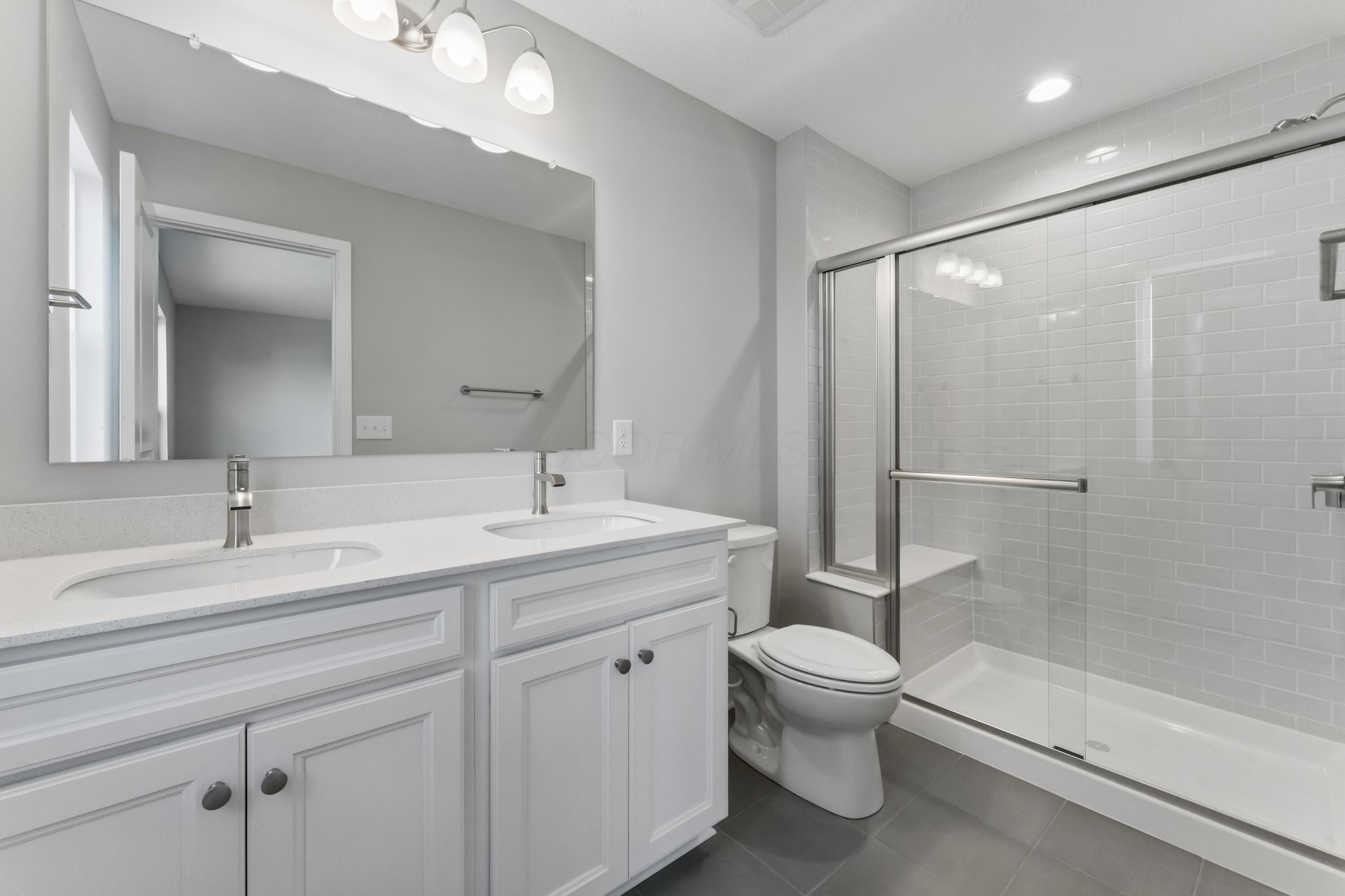 Bathroom with a double vanity and a glass-enclosed white subway-tile shower.