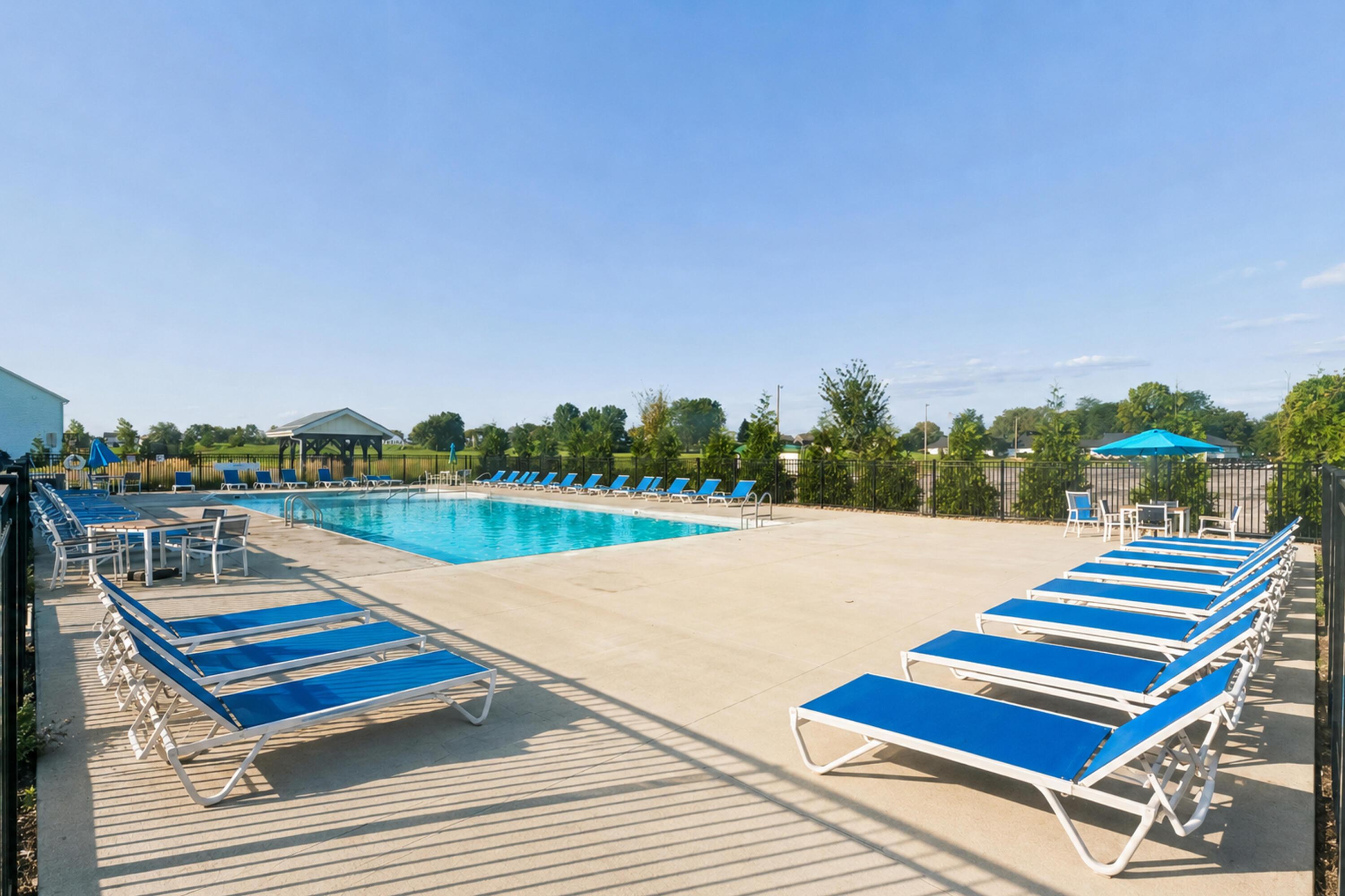 Outdoor swimming pool with blue lounge chairs arranged around a spacious concrete deck.