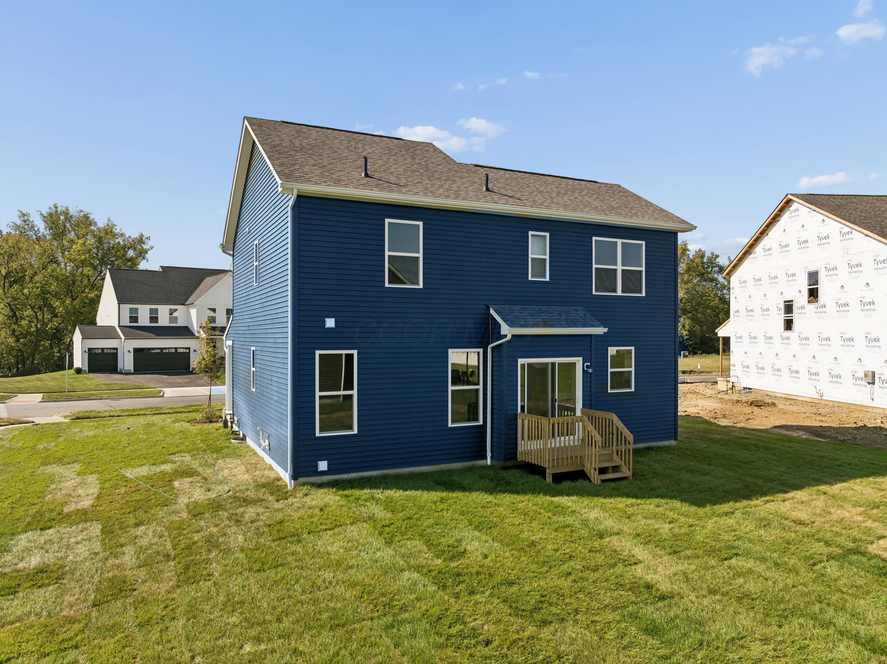 Rear of a navy-blue two-story house with white-trimmed windows, a small wooden deck, and a broad lawn.