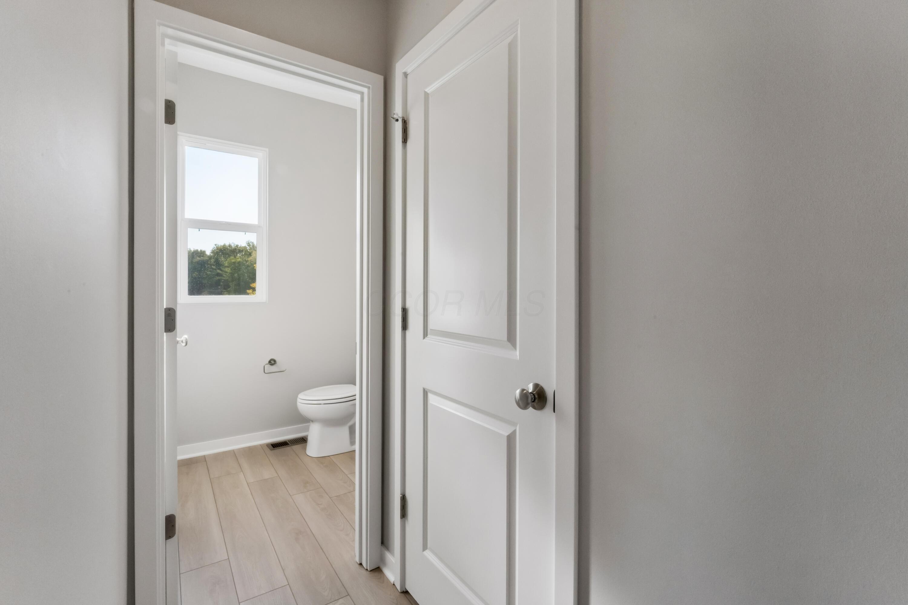Bathroom with a white toilet, light wood-look tile floor, and a window.