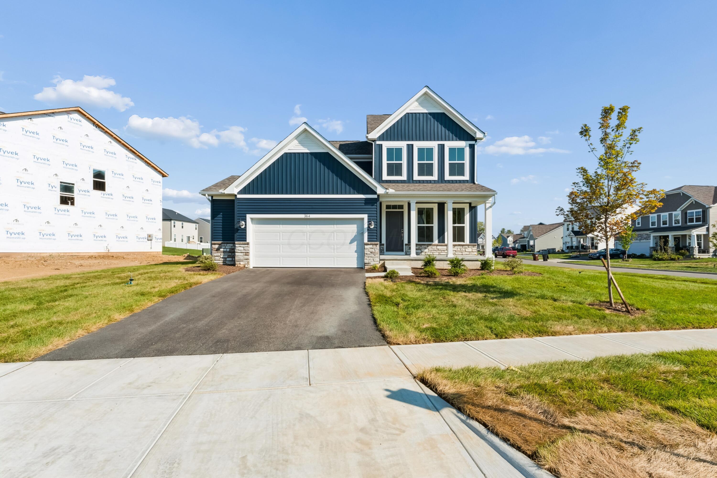 Blue two-story house with a white garage, stone accents, and a neighboring home under construction.