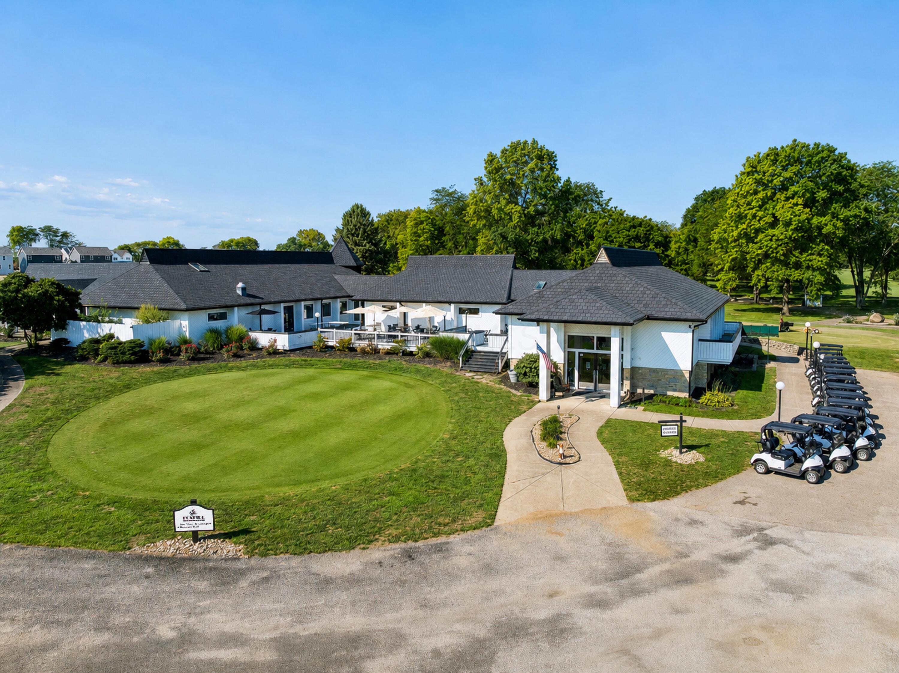 White Foxfire clubhouse with a broad lawn, golf carts, and mature trees.