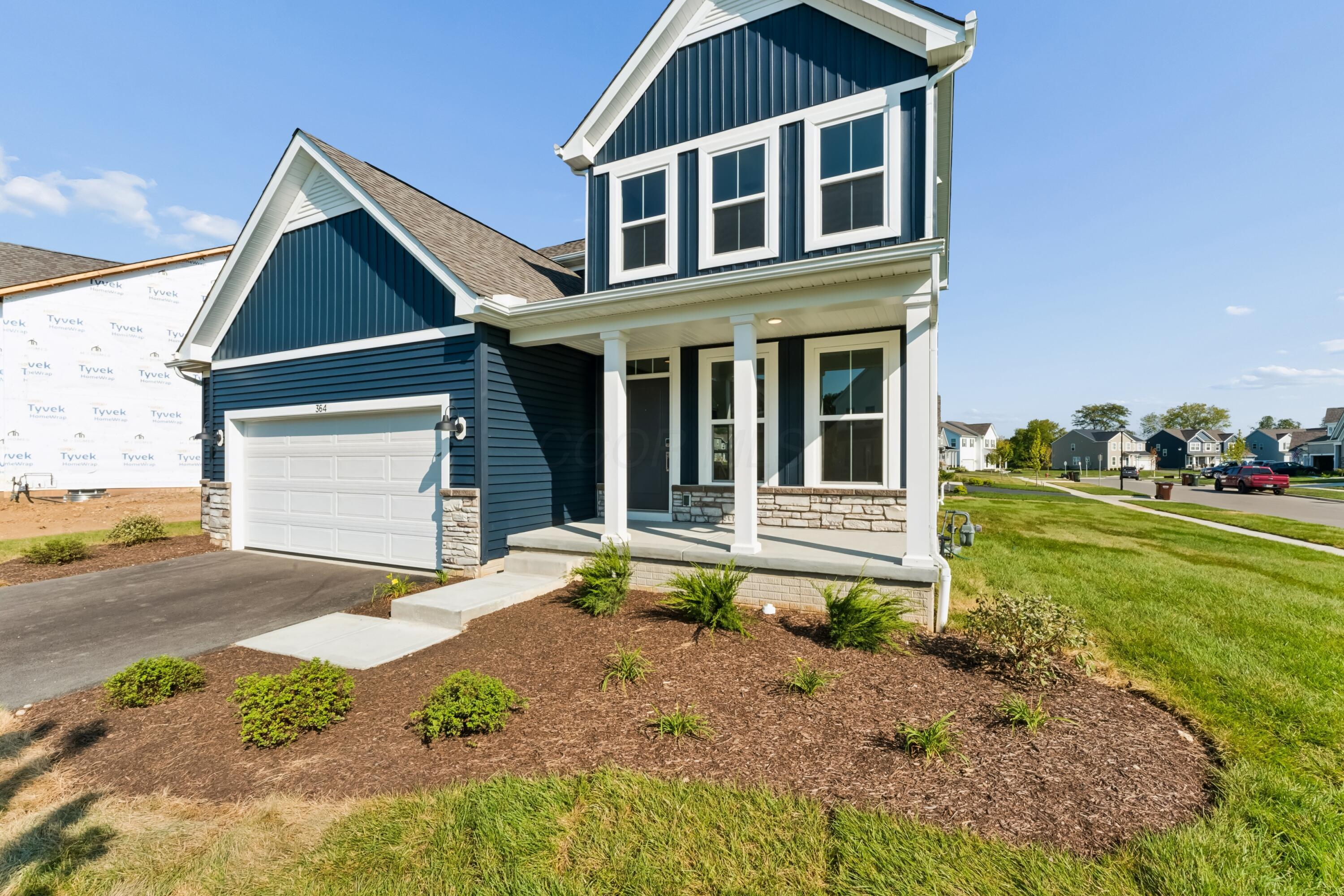 Navy-blue two-story home with white trim, stone accents, and a covered porch beside its attached garage.