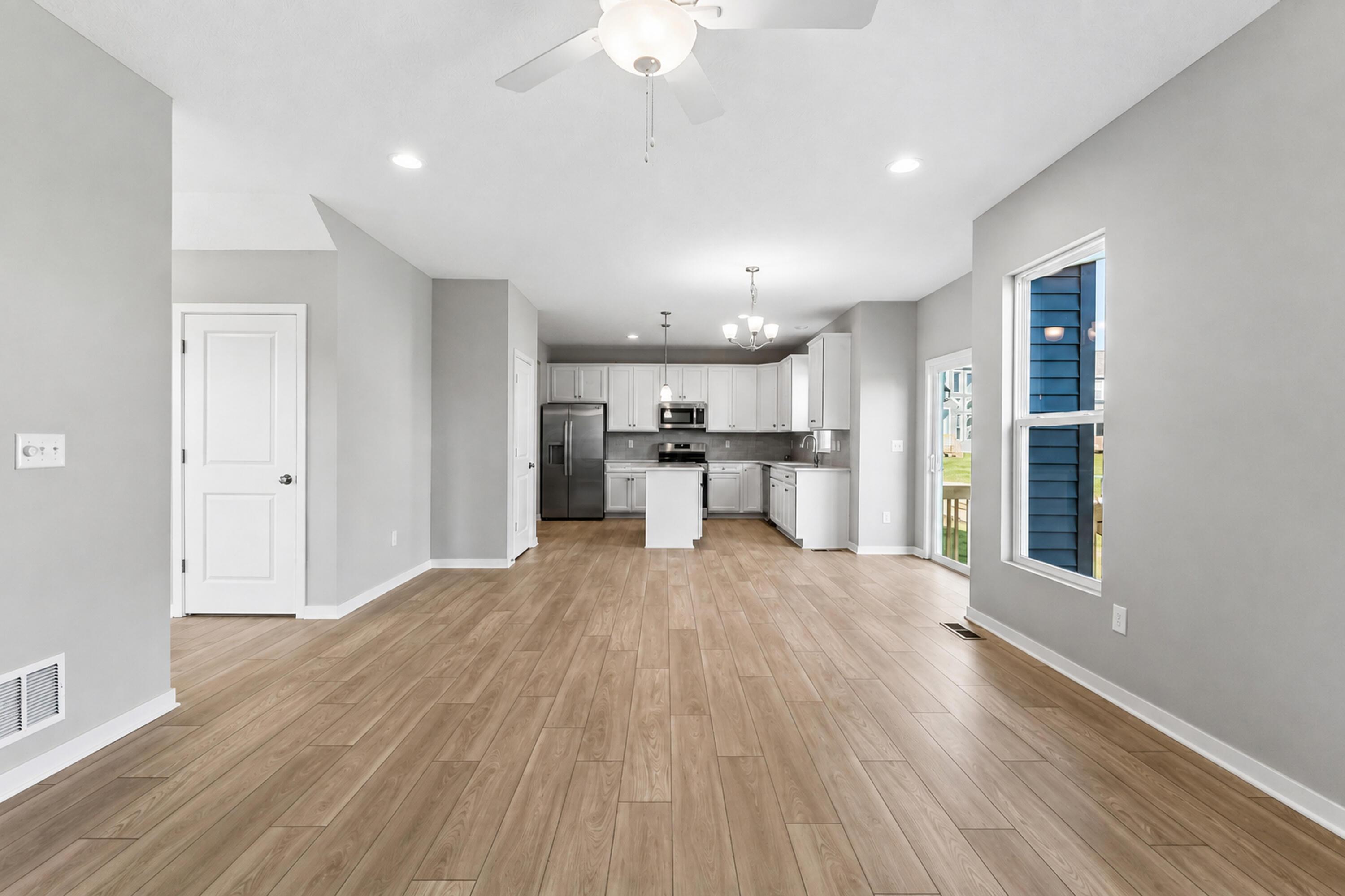 Open-plan living area and kitchen with white cabinets, stainless steel appliances, and wood-look floors.