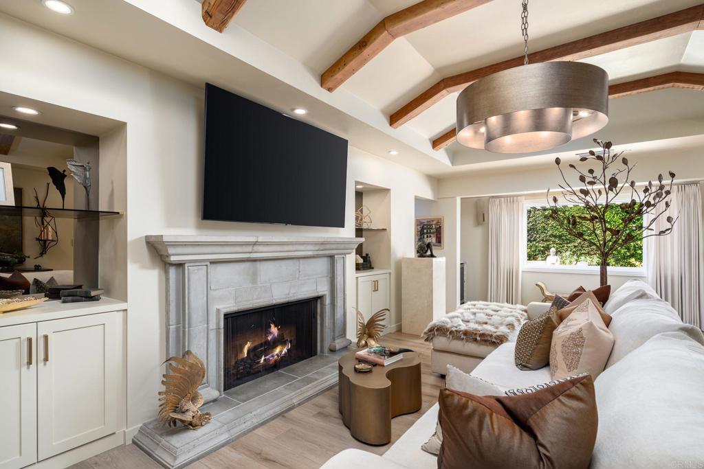 Living room with a stone fireplace, white sectional, mounted television, and exposed wood ceiling beams.