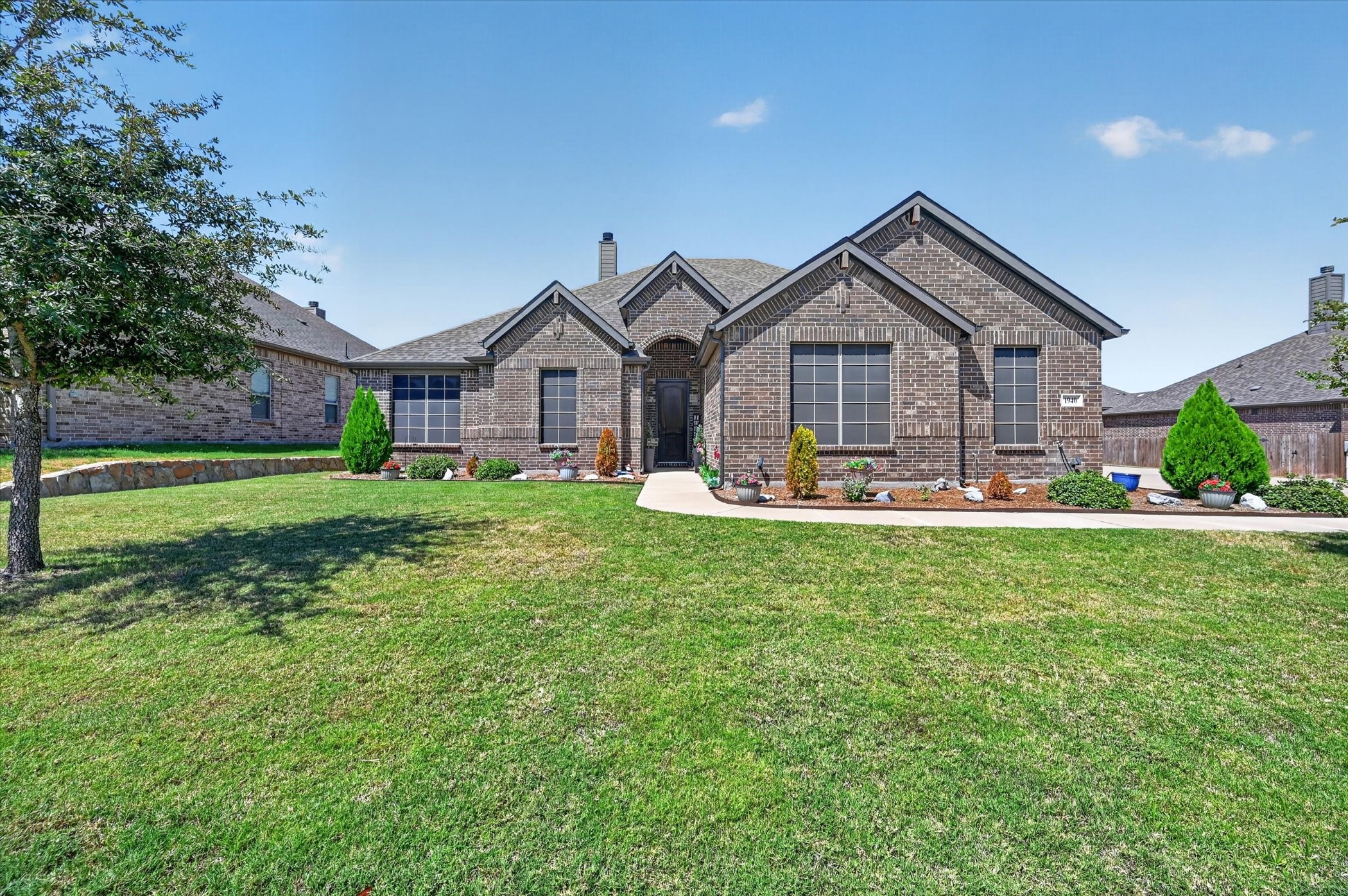 Brick house with multiple gables, a broad lawn, and landscaped flower beds.