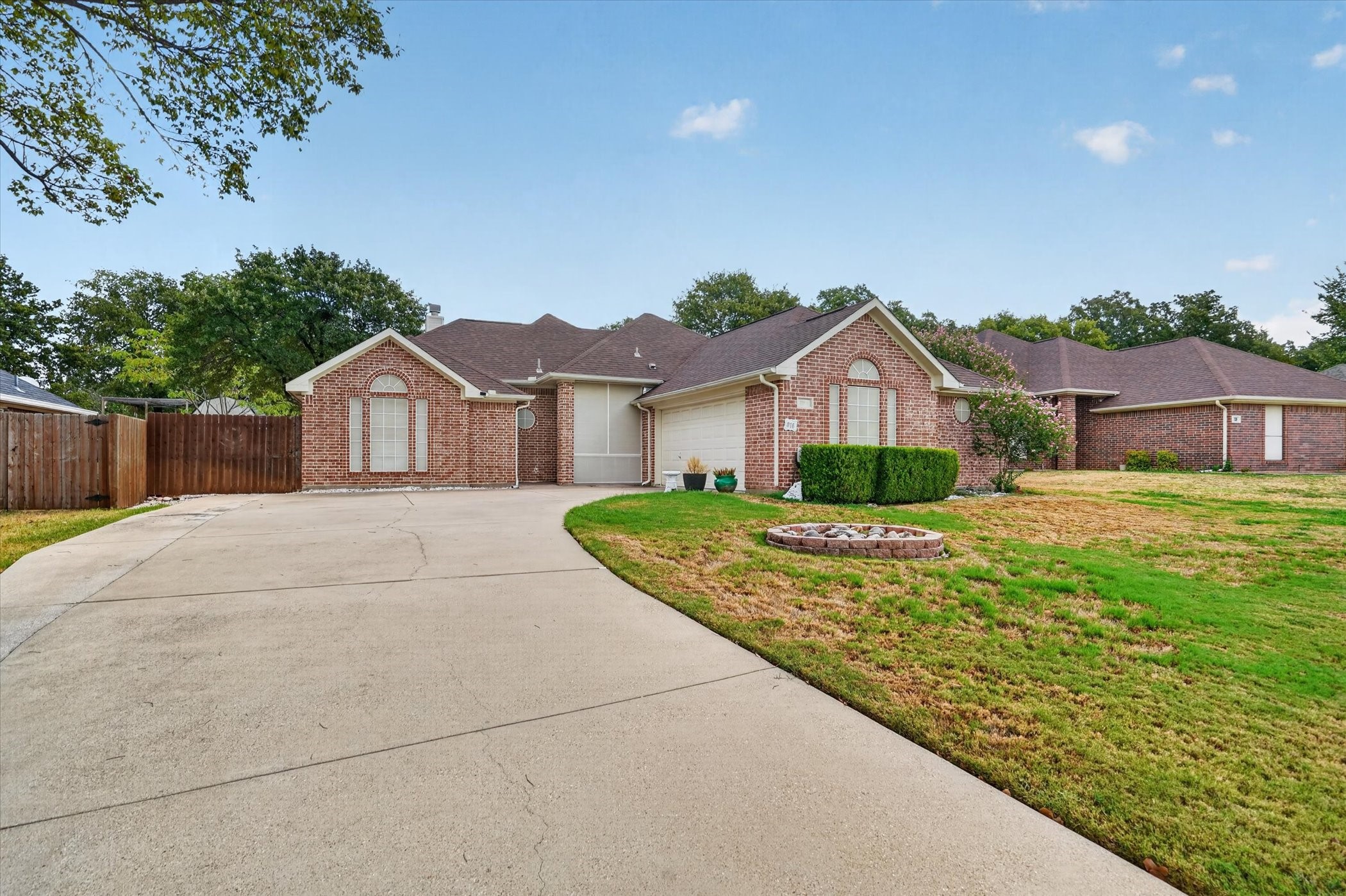Red brick house with an attached garage, wide curved driveway, and patchy front lawn.