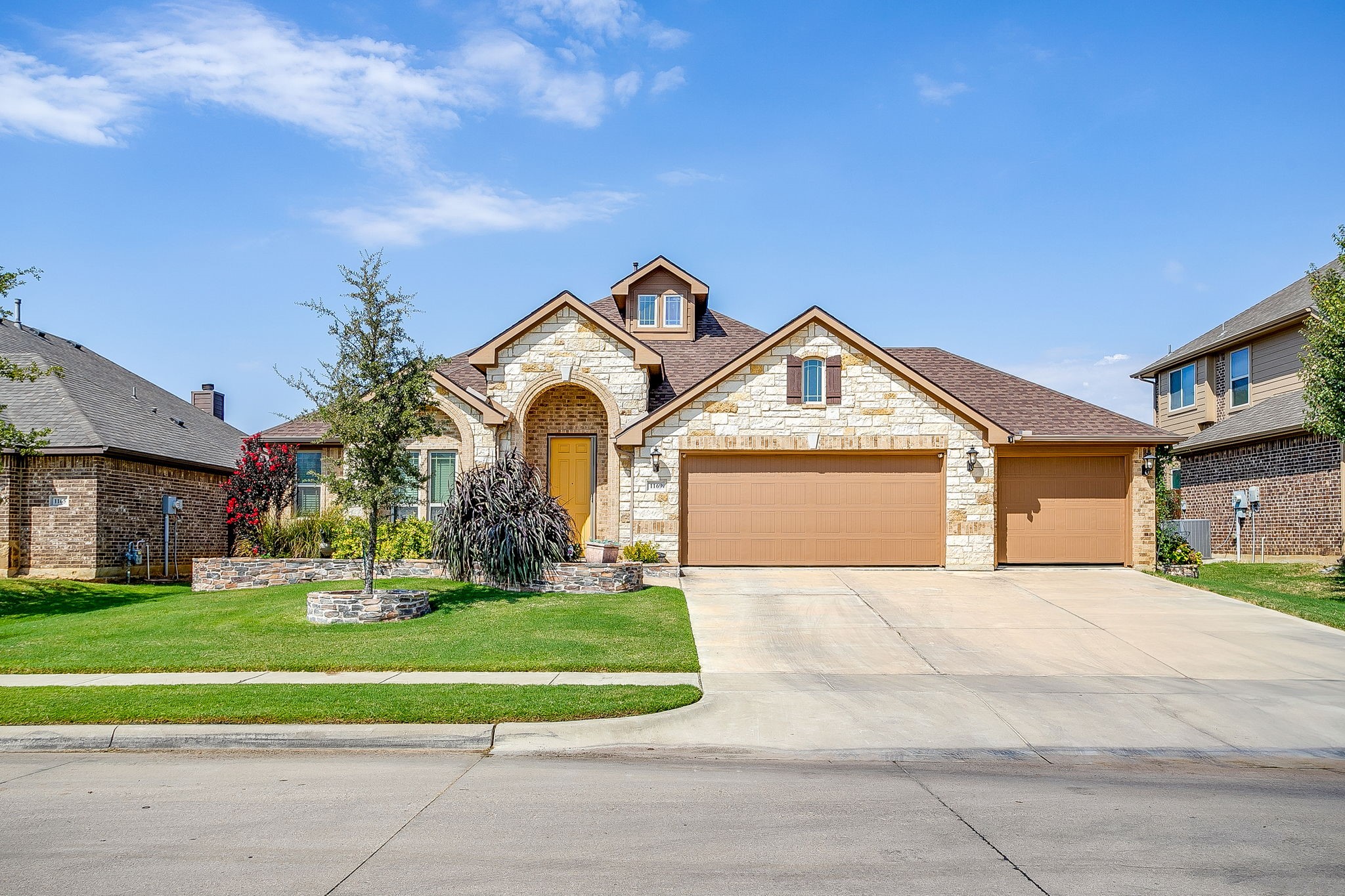Stone-front house with an arched entry, yellow door, and three-car garage.