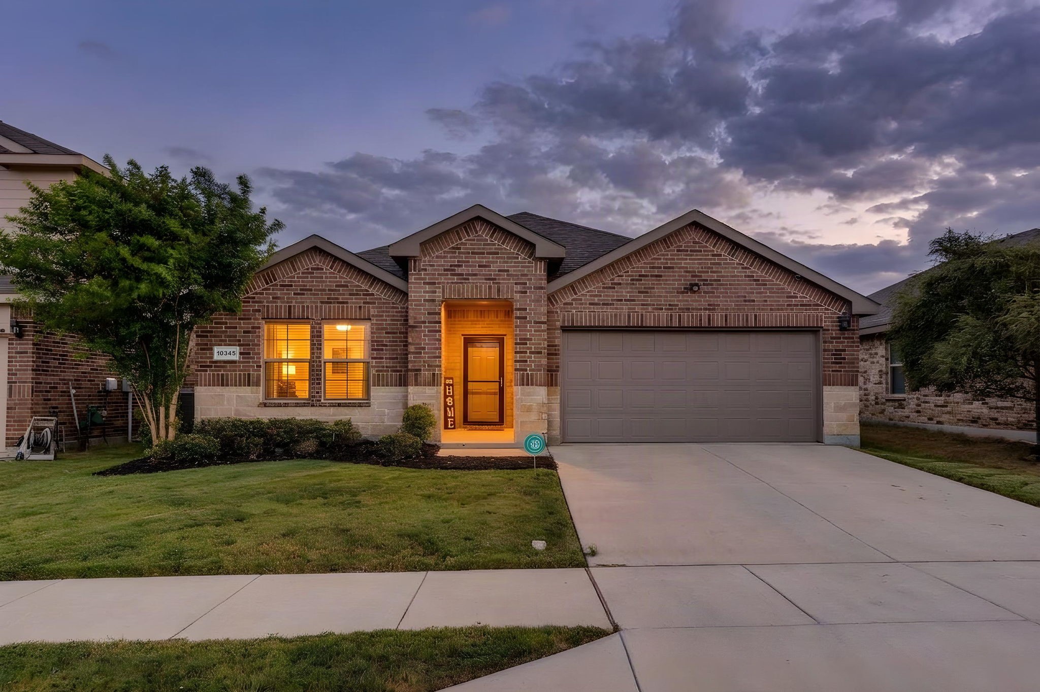 Brick home with a two-car garage and warmly lit entryway at dusk.