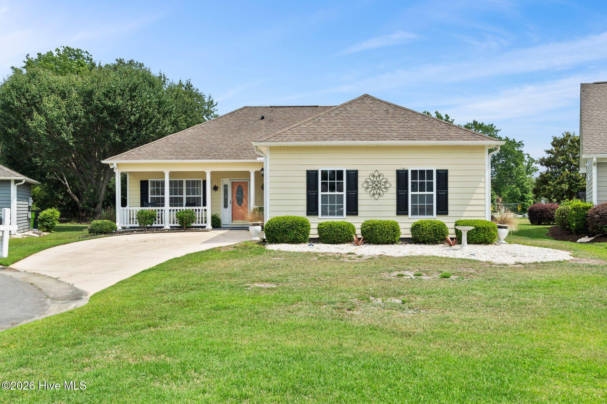 Cream-colored single-story home with a covered porch, black shutters, and curved driveway.