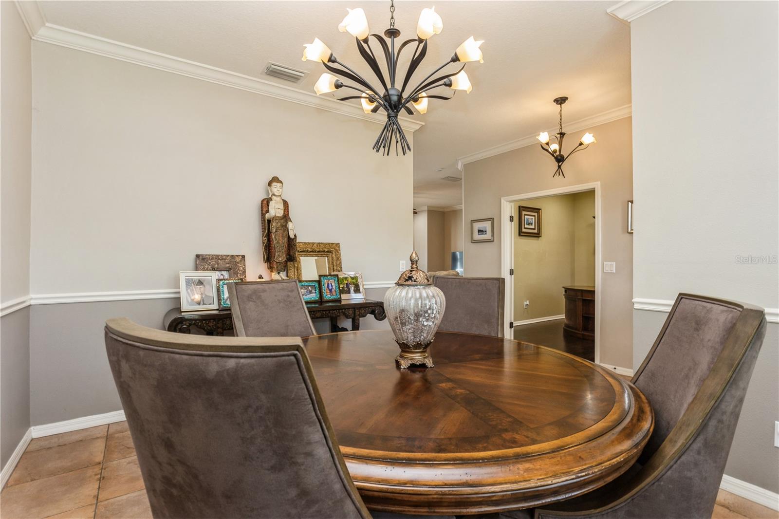 Dining room with a round wooden table, upholstered chairs, and two decorative chandeliers.