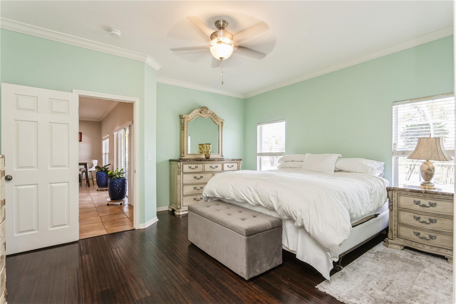 Bedroom with a white bed, mint-green walls, dark wood floors, and a ceiling fan.