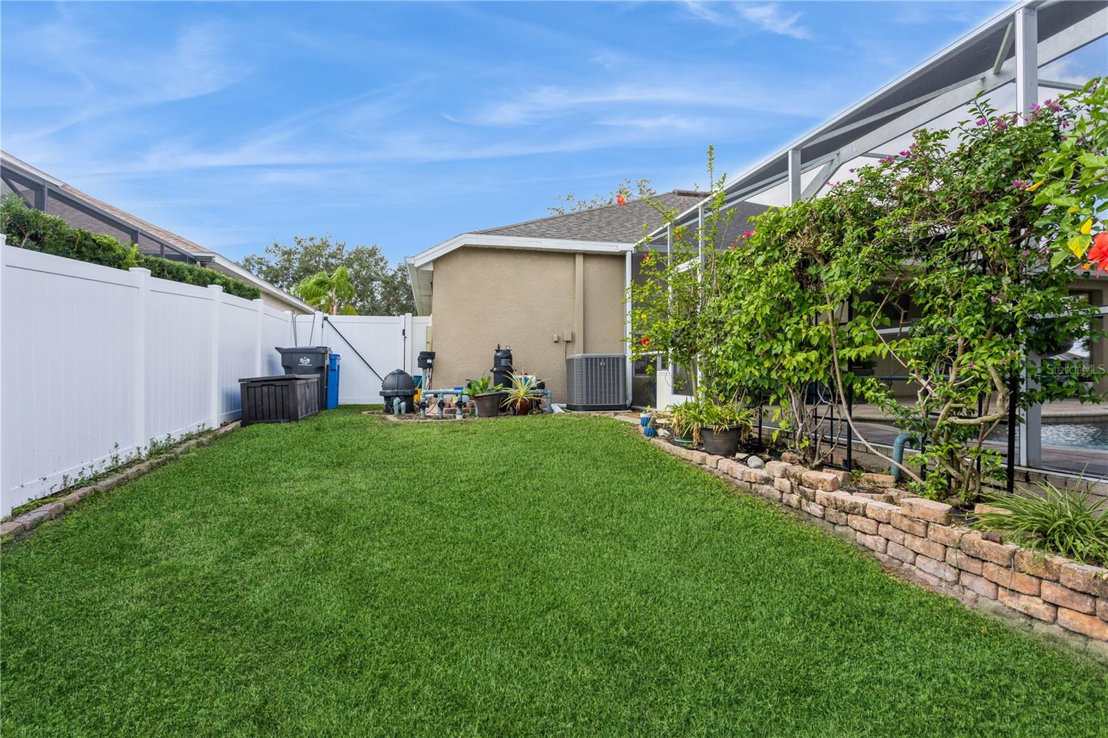 Backyard lawn bordered by a white privacy fence, with a vine-covered screened pool enclosure.