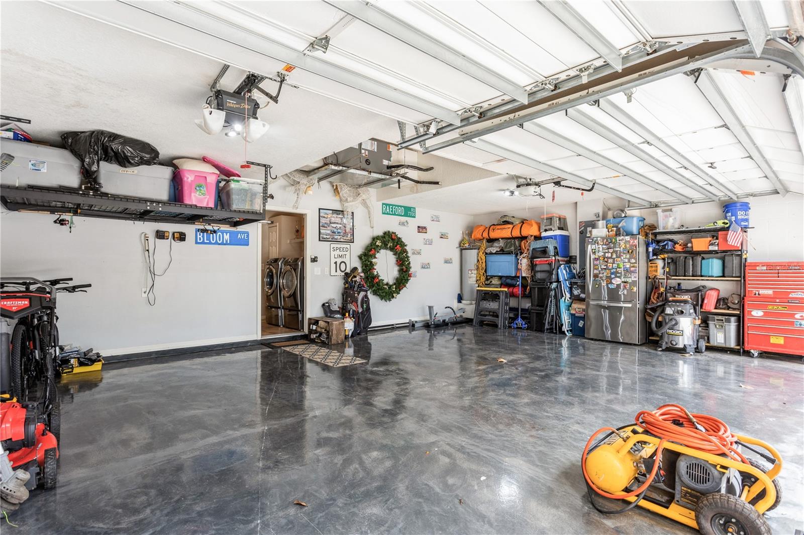 Spacious garage with a glossy concrete floor, overhead storage, tools, and open garage doors.