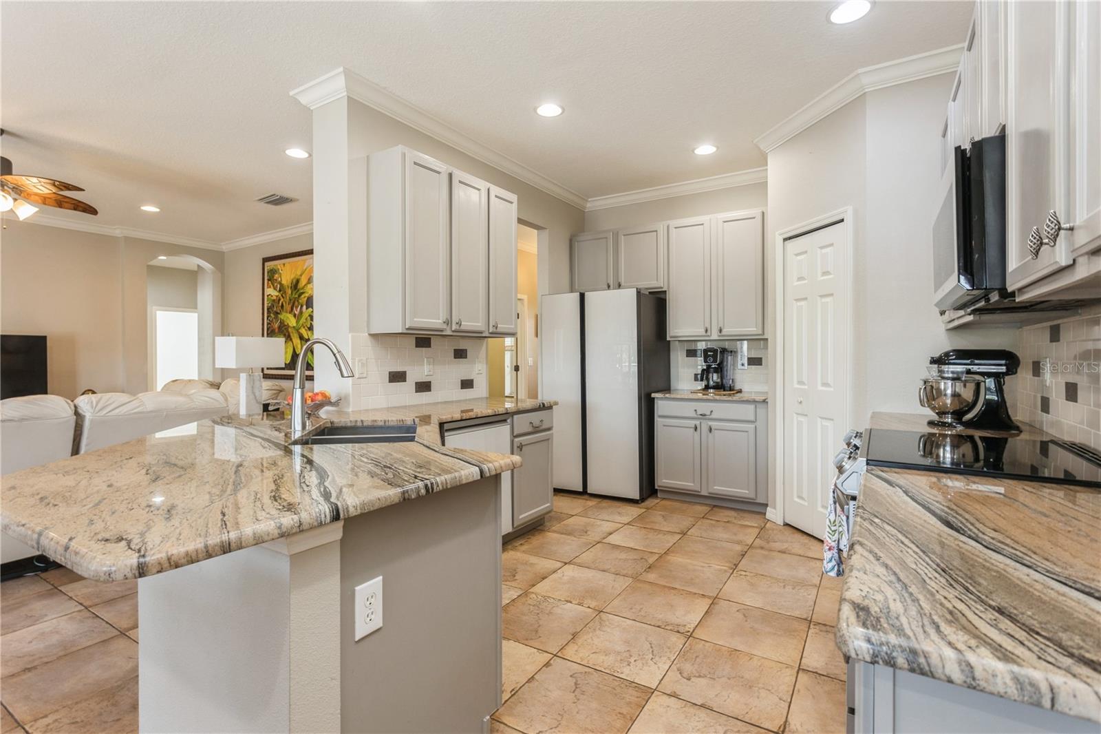 Kitchen with a granite island and sink, gray cabinets, stainless steel refrigerator, and tiled floors.