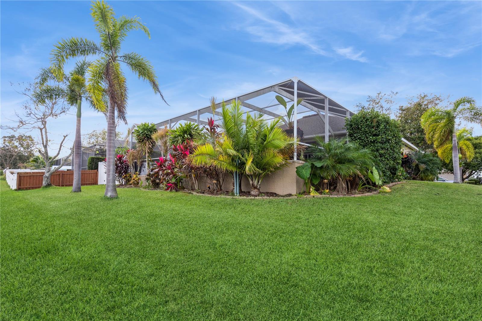 Home exterior with a screened enclosure, tropical landscaping, palm trees, and a broad lawn.