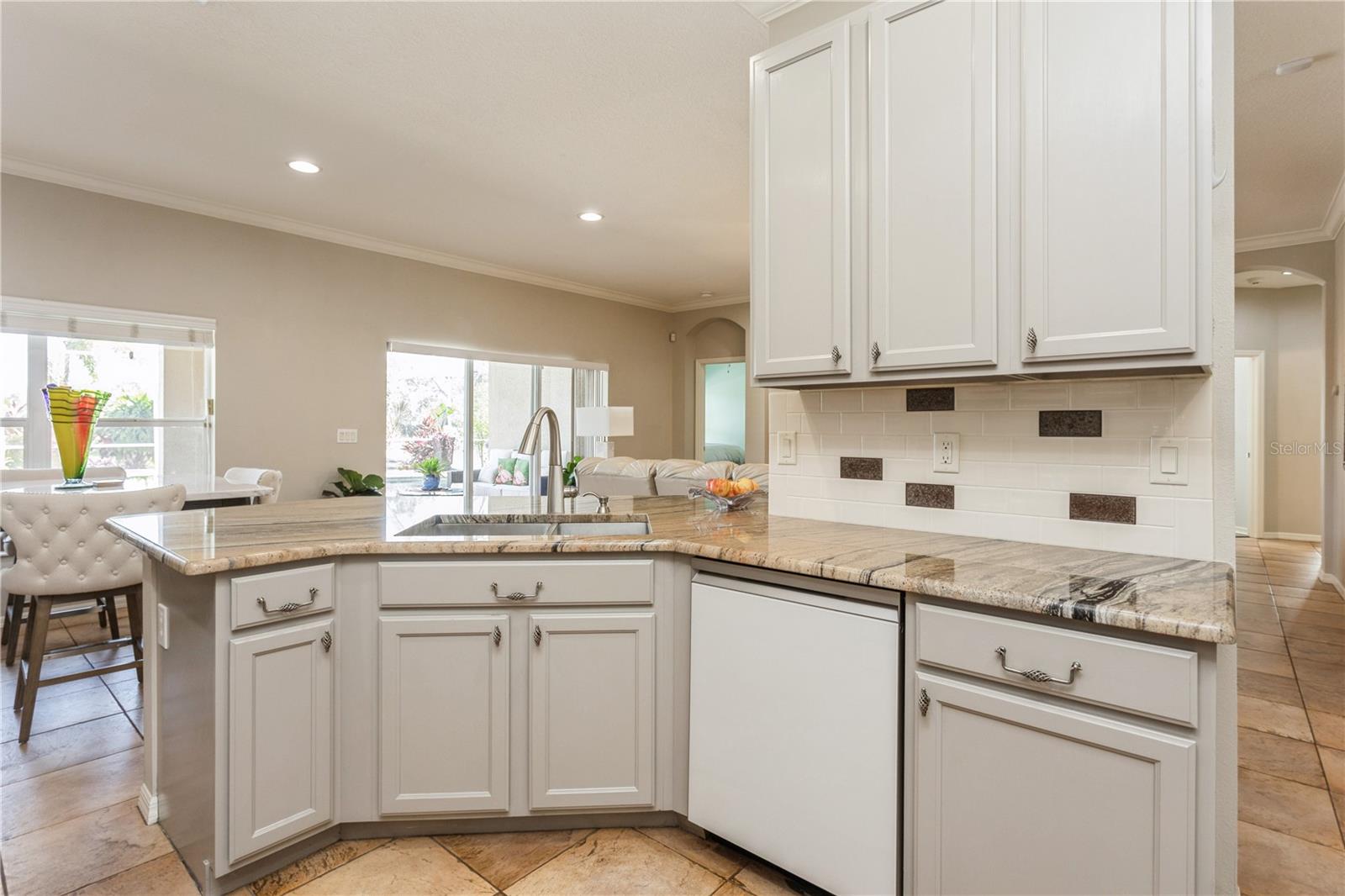 Kitchen with a granite island, white cabinets, and tile backsplash opening to the living and dining areas.