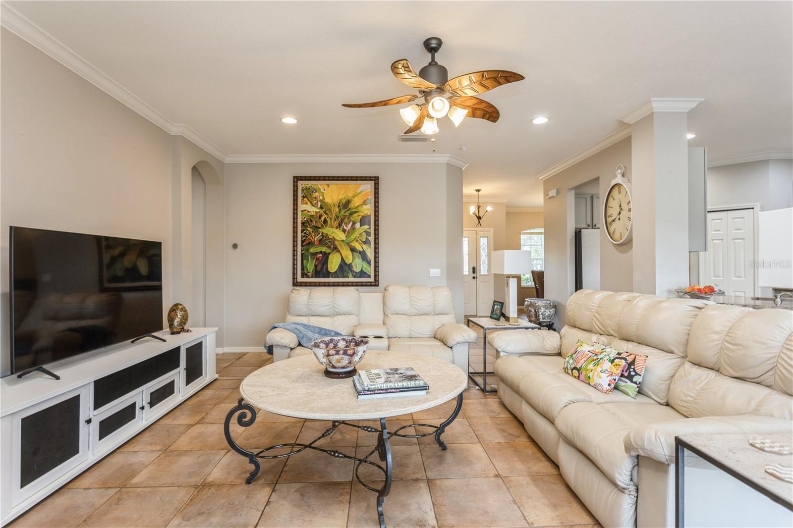 Living room with cream leather sofas, tan tile floors, and a wood-blade ceiling fan.