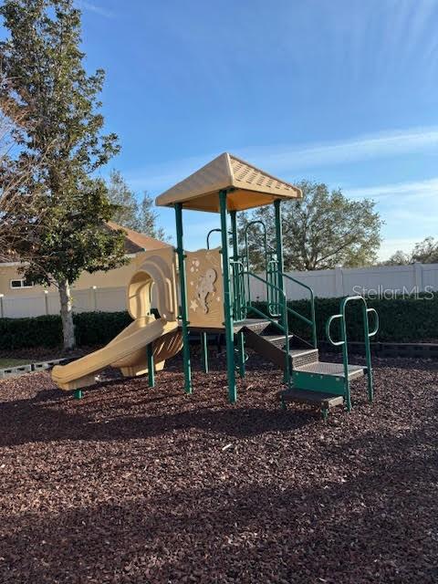 Community playground with a tan slide and green climbing structure on wood chips.