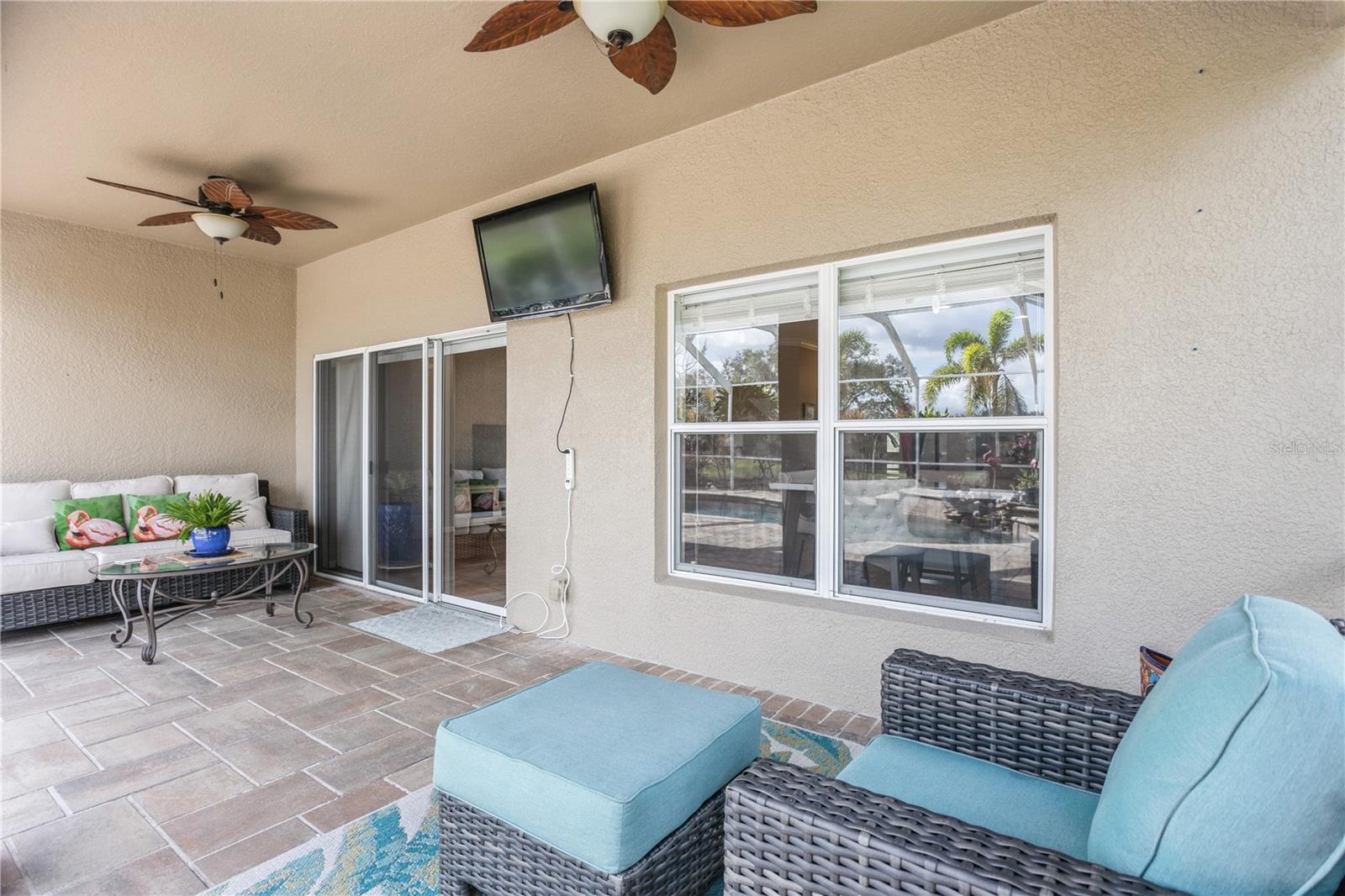 Covered patio with wicker seating, tiled floor, ceiling fans, and views toward the pool.
