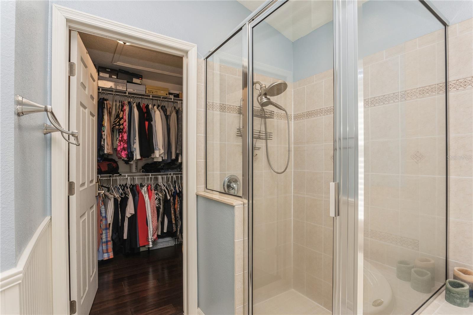 Bathroom with a glass shower beside an open walk-in closet filled with clothes.