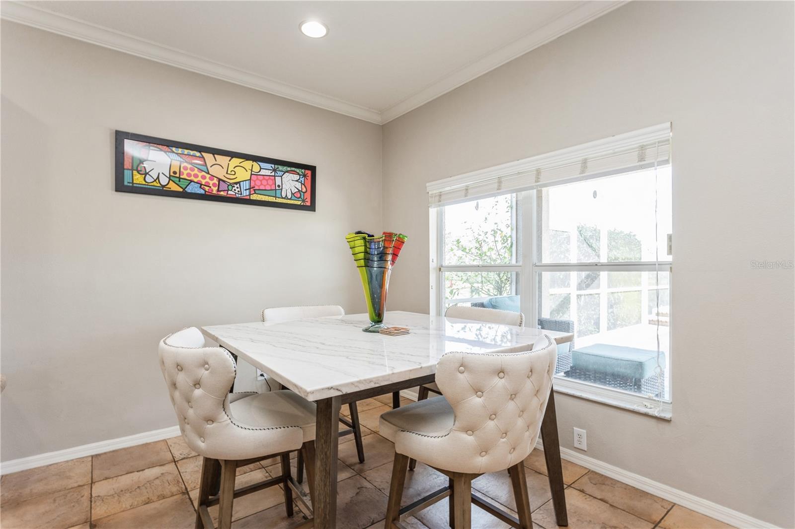 Dining room with a marble-top table, cream tufted chairs, and a large window.