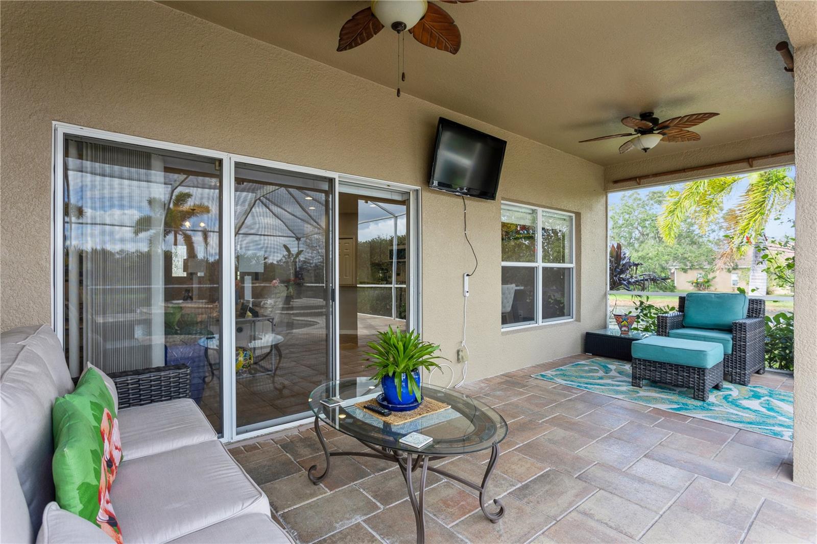 Covered patio with tiled flooring, wicker seating, ceiling fans, and a view of the green yard.