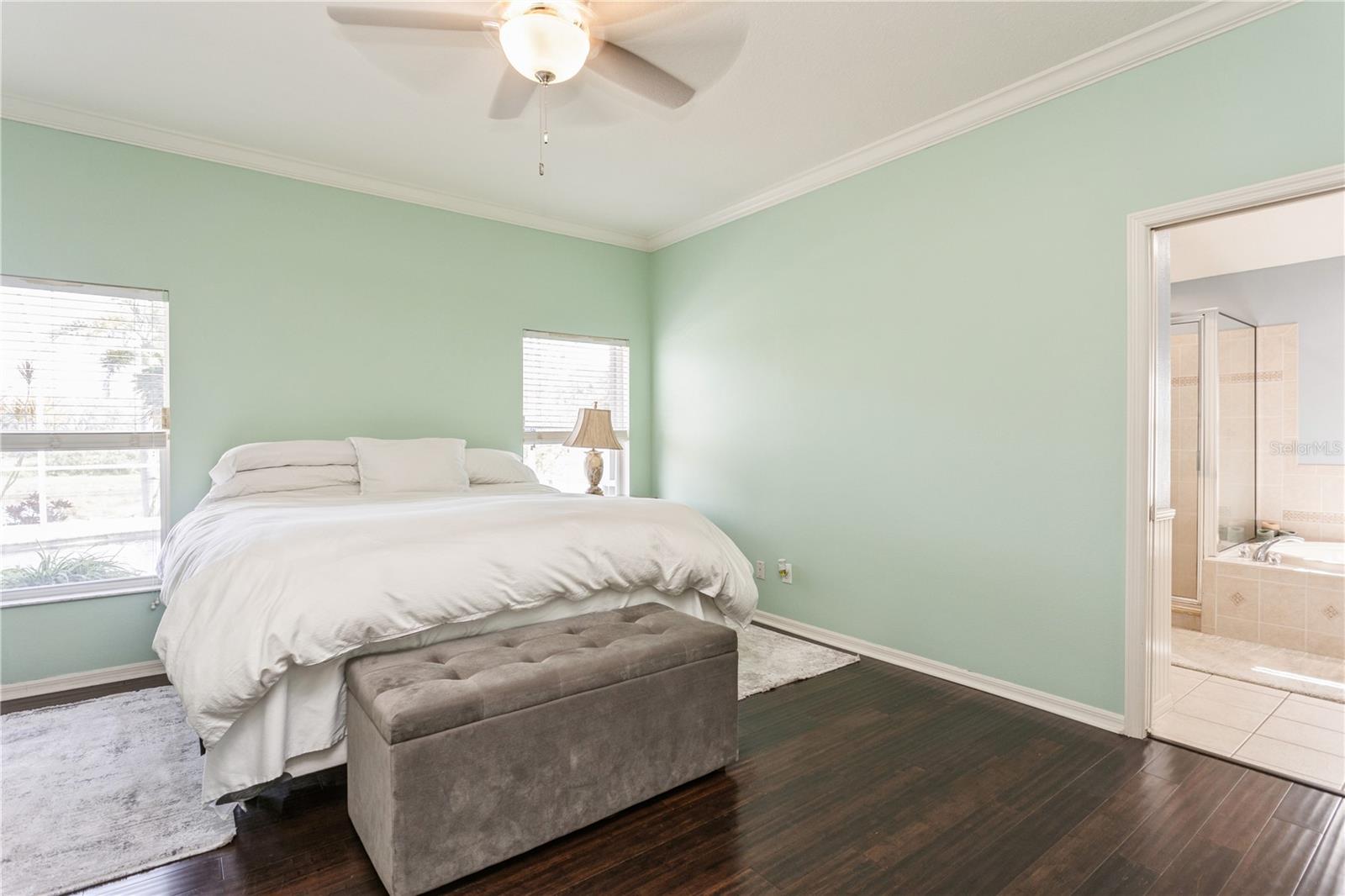 Bedroom with mint-green walls, a white bed, gray bench, and doorway to an en-suite bathroom.