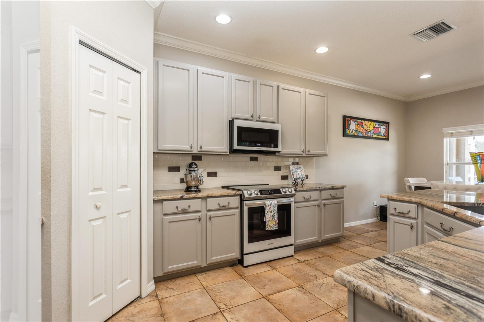 Kitchen with gray cabinets, granite counters, stainless steel appliances, and a large foreground island.