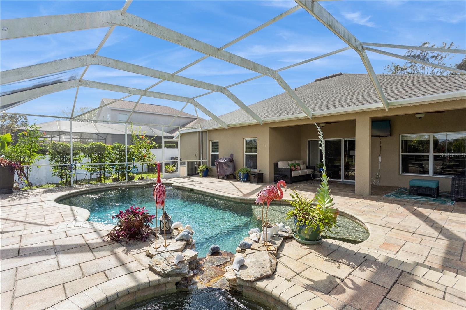 Backyard pool beneath a screened enclosure, with a rock waterfall and covered patio.