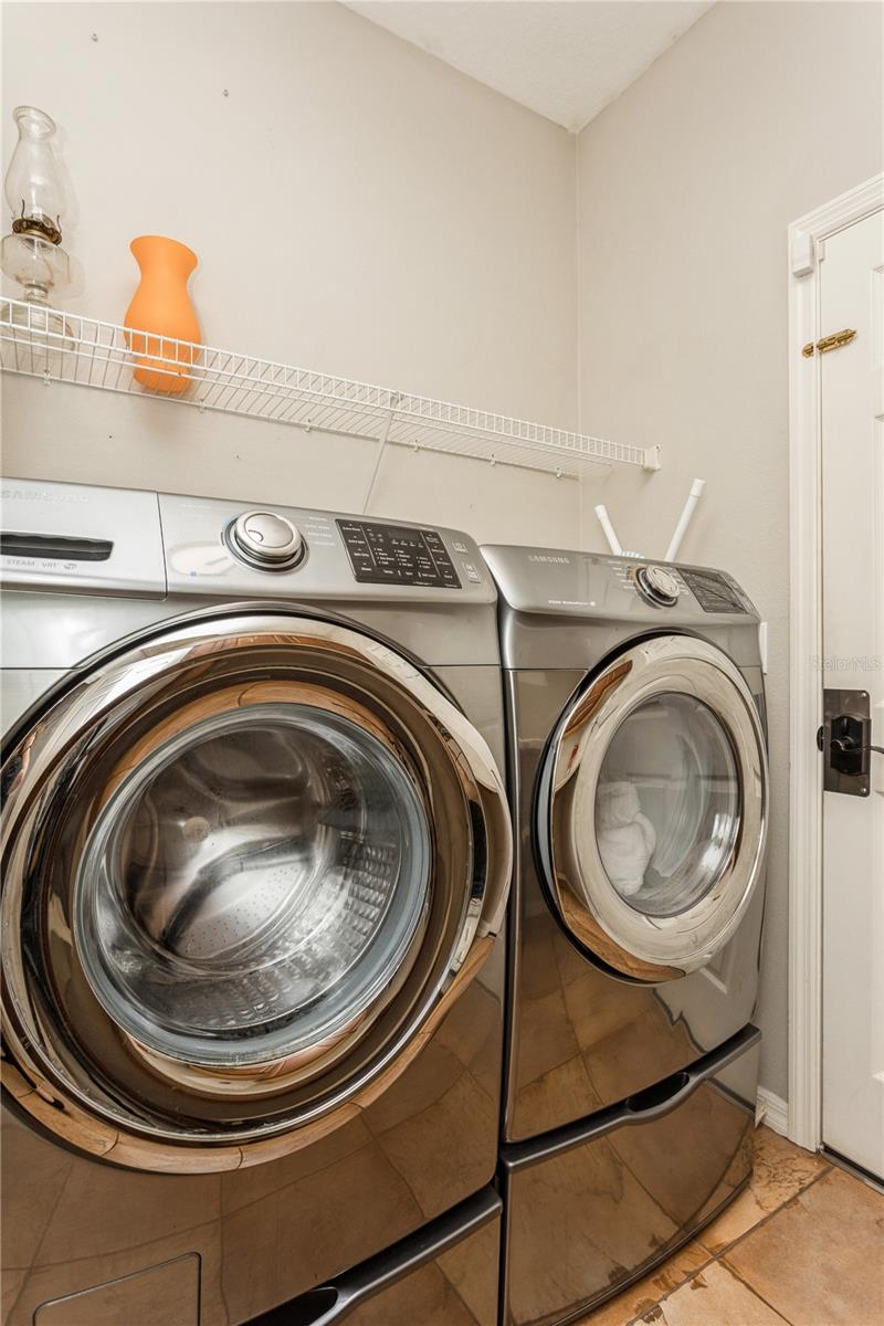 Laundry room with stainless-steel front-loading washer and dryer beneath a white wire shelf.