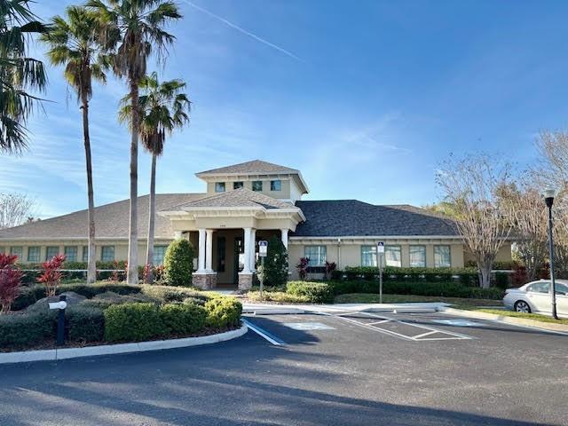 Community building with a covered entrance, palm trees, and parking spaces in front.