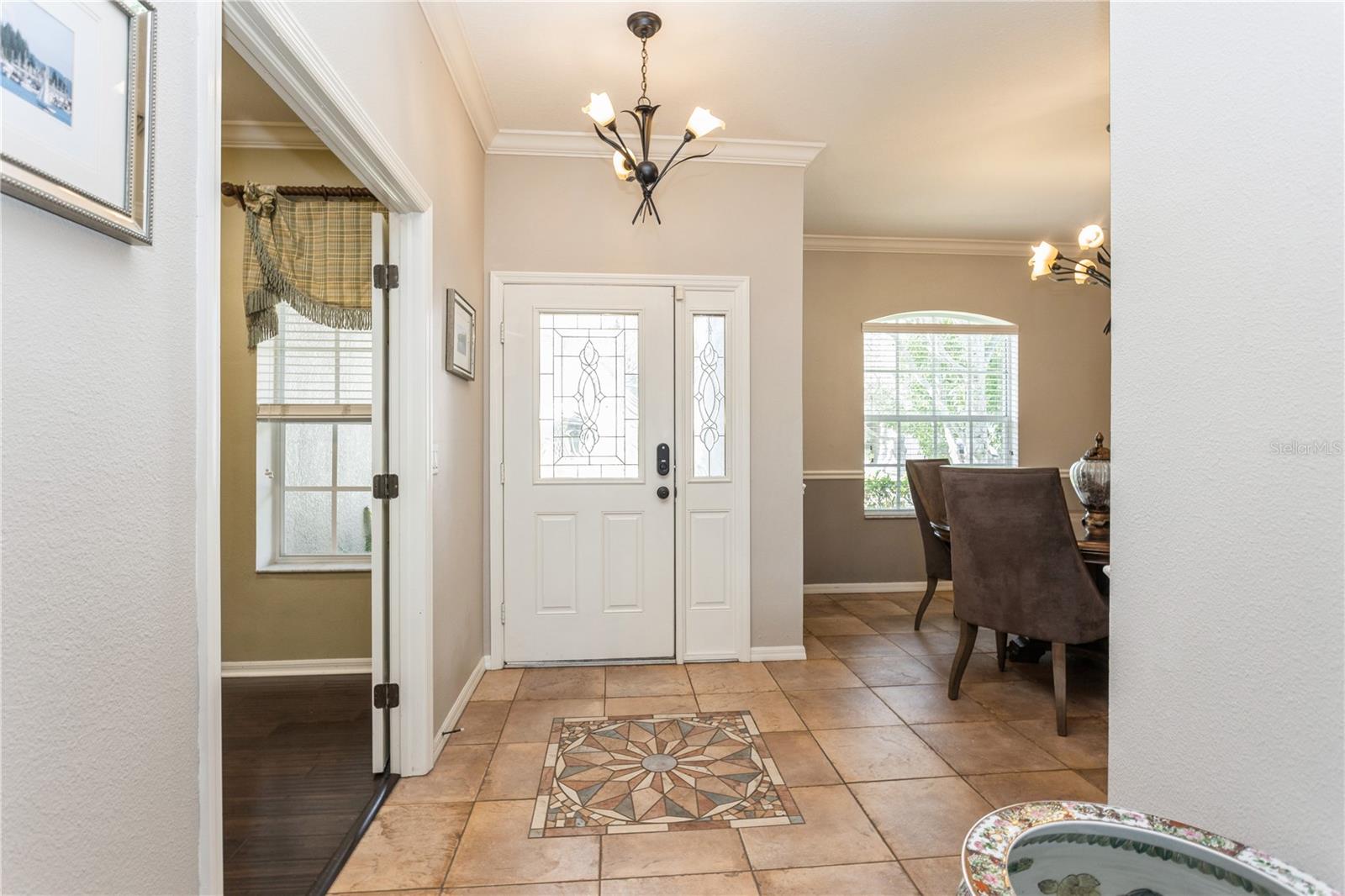 Entry foyer with a glass-panel front door, tiled floor with compass medallion, and dining room beyond.