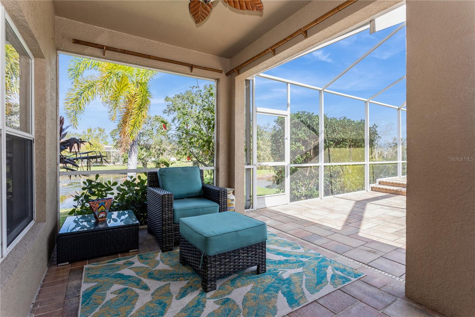 Screened lanai with wicker seating and a pond view.