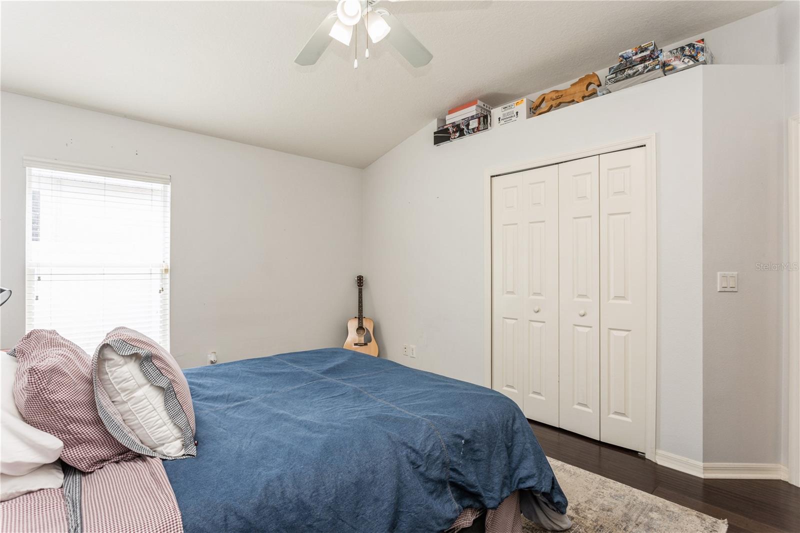 Bedroom with a blue-covered bed, white closet doors, and a guitar by the wall.
