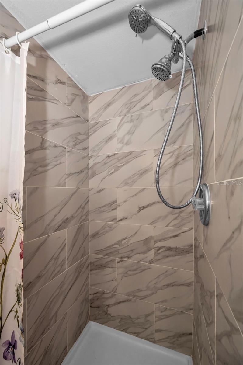 Shower stall with marble-look tile and a chrome handheld showerhead.