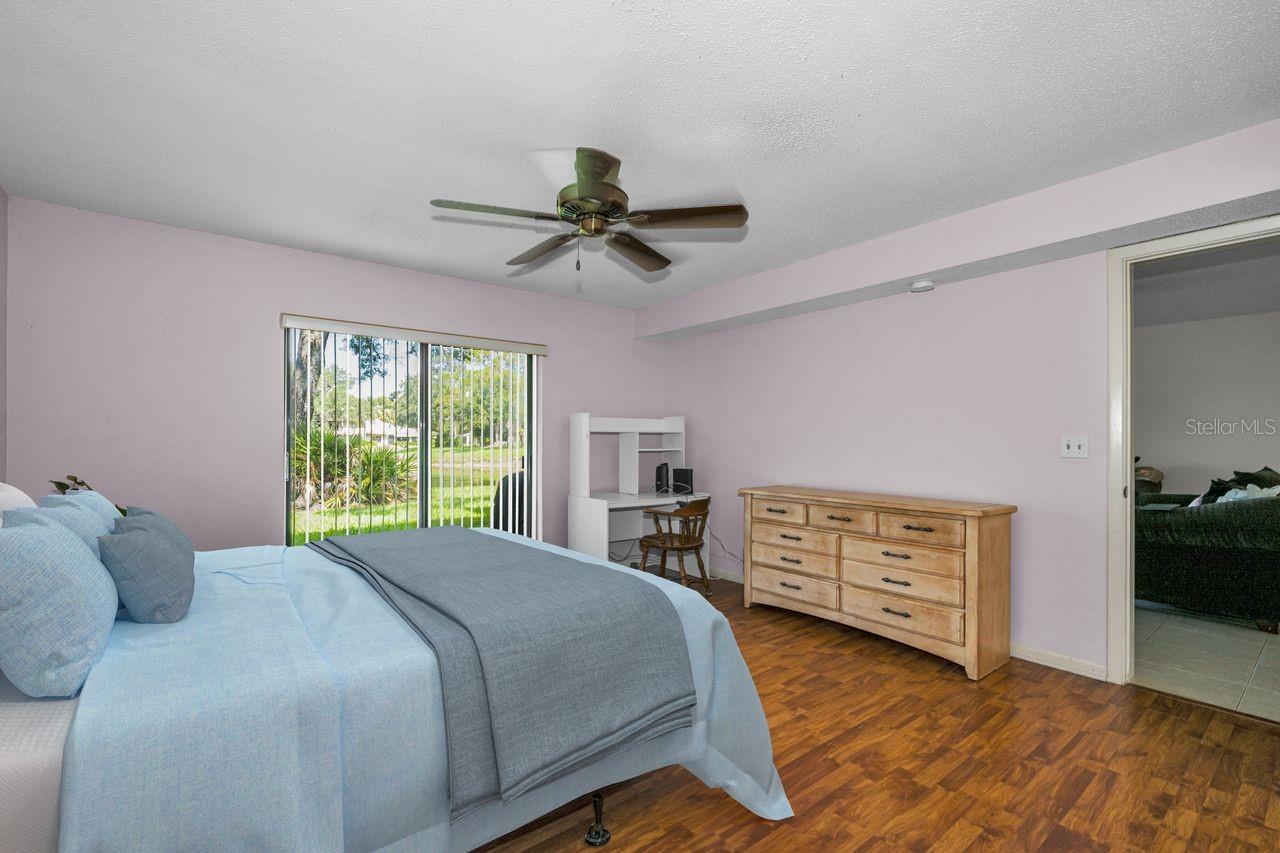 Furnished bedroom with a blue bed, wooden dresser, and sliding doors overlooking a lawn.