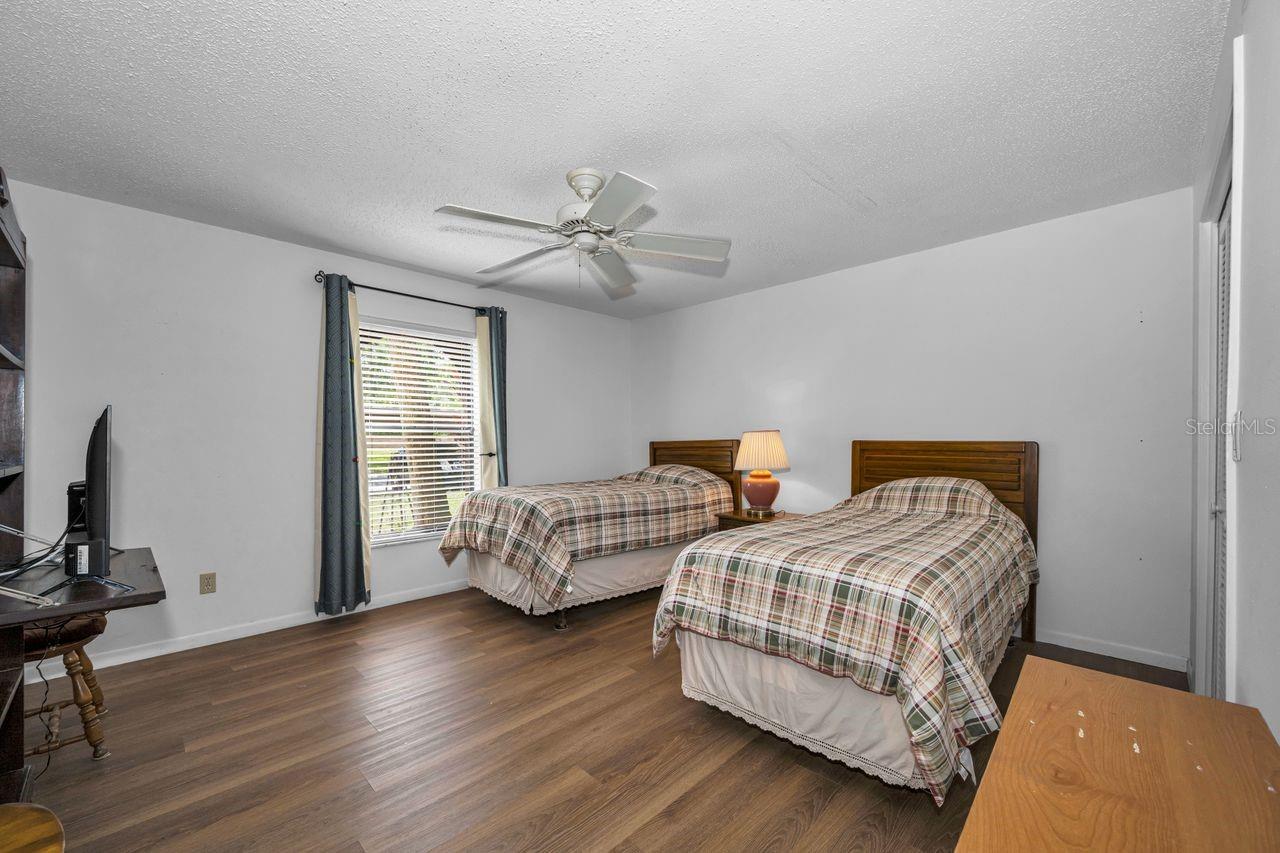 Bedroom with two plaid-covered twin beds, a window with blinds, and wood-look flooring.