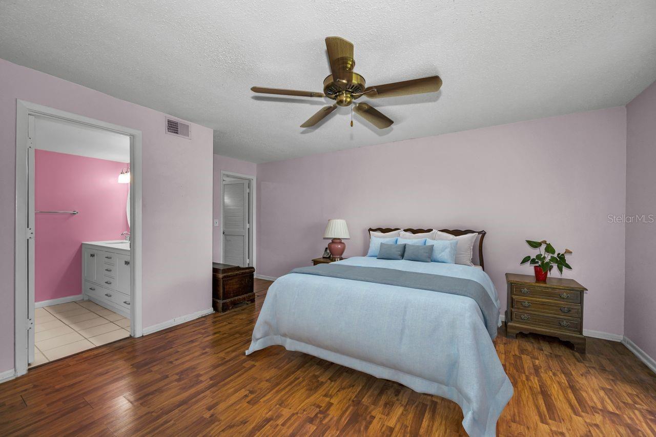 Bedroom with a light blue bedspread, hardwood floors, and an open doorway to a pink bathroom.