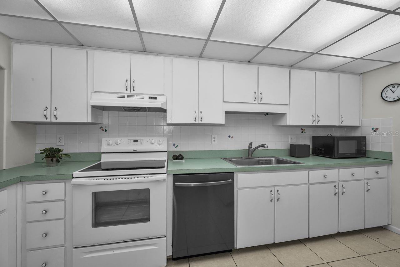 Kitchen with white cabinets, pale green countertops, and a white range beside a dark dishwasher.