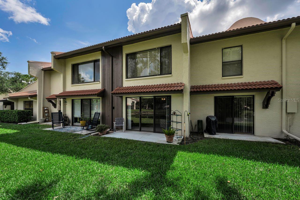 Rear exterior of a two-story condo with sliding glass doors, a small patio, and a green lawn.