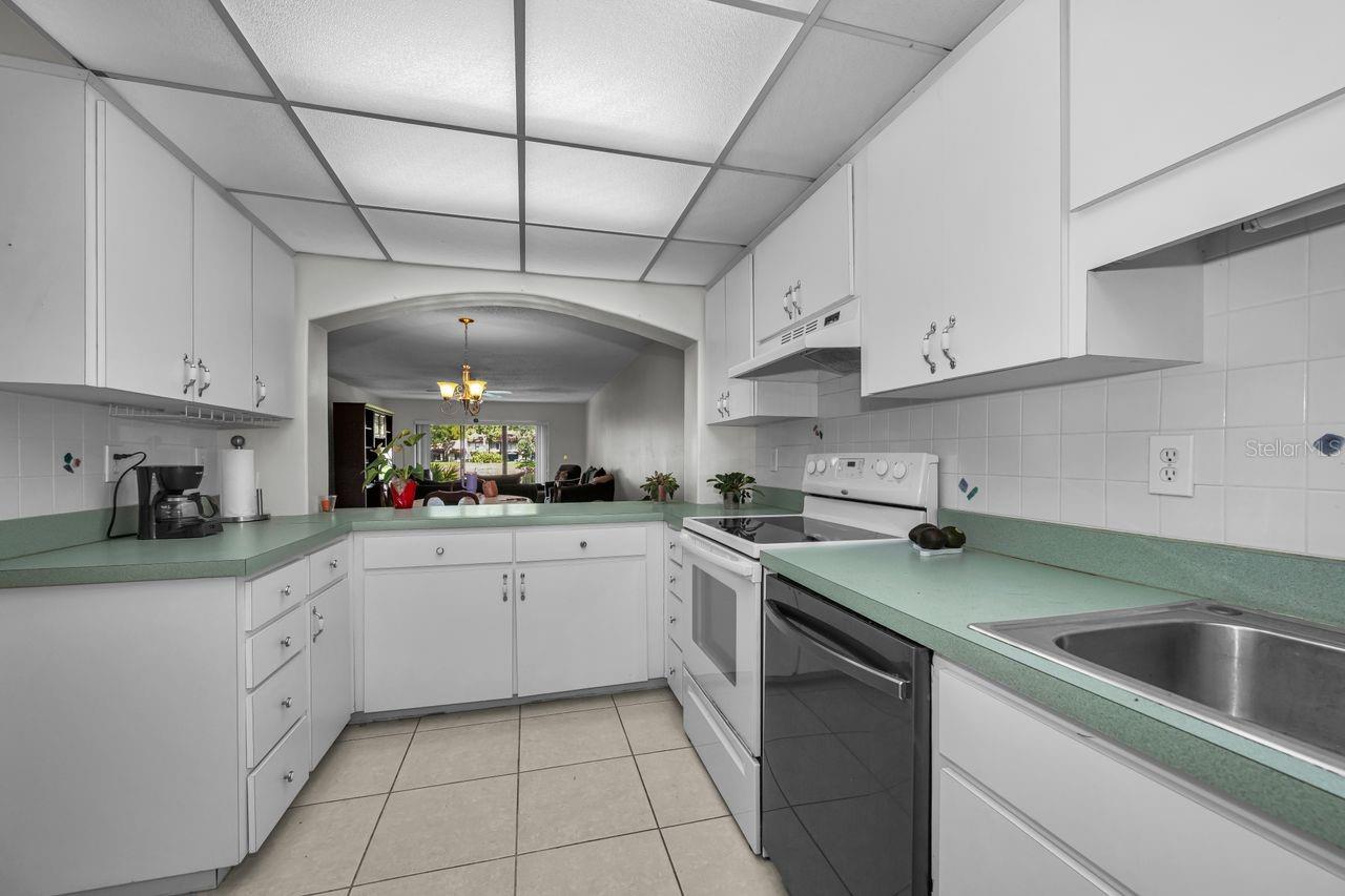 Kitchen with white cabinets, pale green countertops, and an arched opening to the living room.