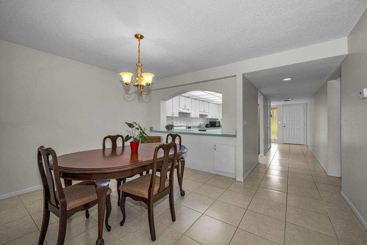 Dining area with a dark wood table, open kitchen pass-through, and tiled hallway.