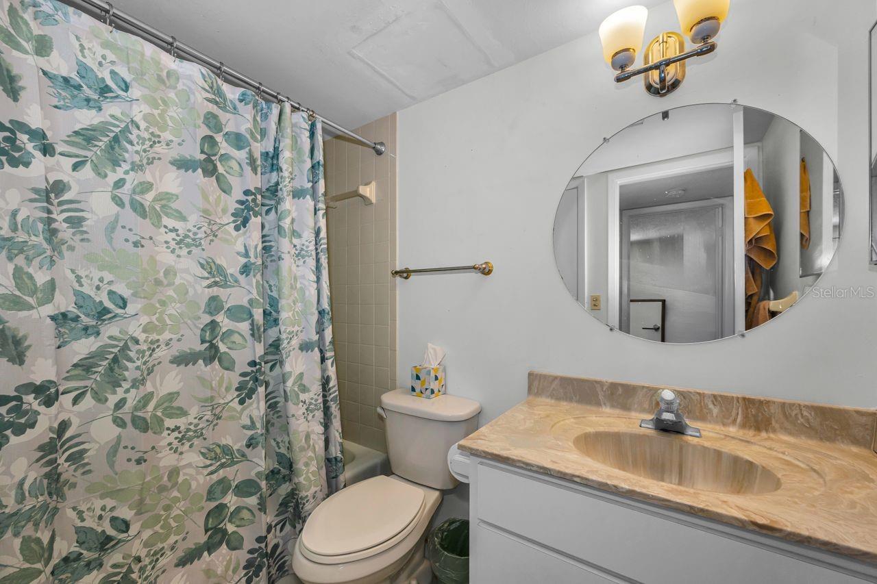 Bathroom with a floral shower curtain, round mirror, and marble-look vanity.