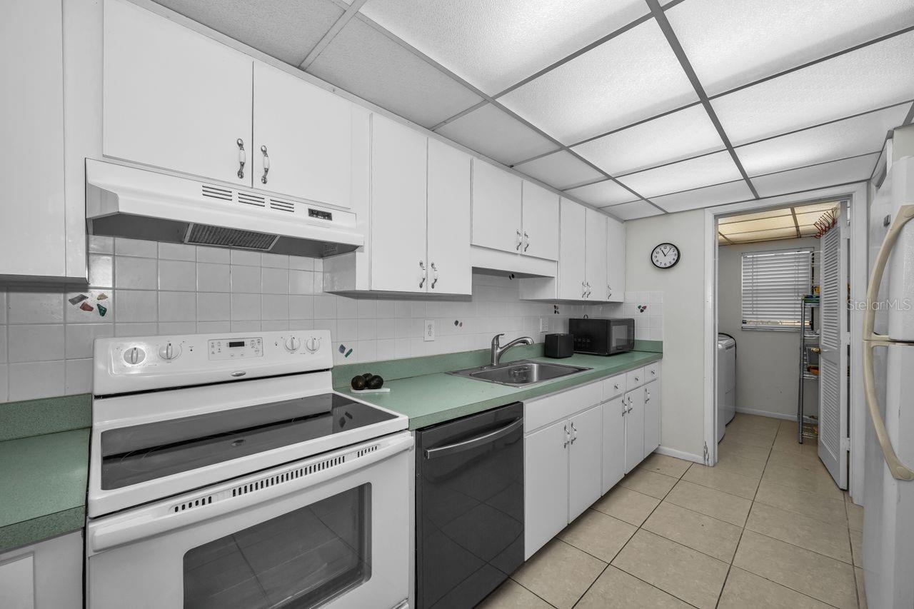 Kitchen with white cabinets, pale green counters, and a doorway to the laundry area.