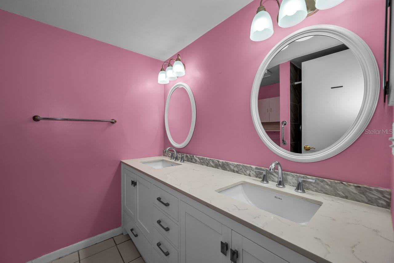 Bathroom with a white double-sink vanity, pink walls, oval mirrors, and chrome fixtures.